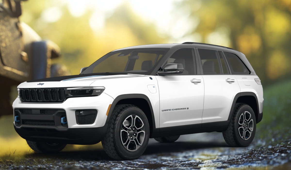 White Jeep Grand Cherokee 4xe Trailhawk plug-in hybrid SUV with black roof and blue tow hooks, parked on a forest trail